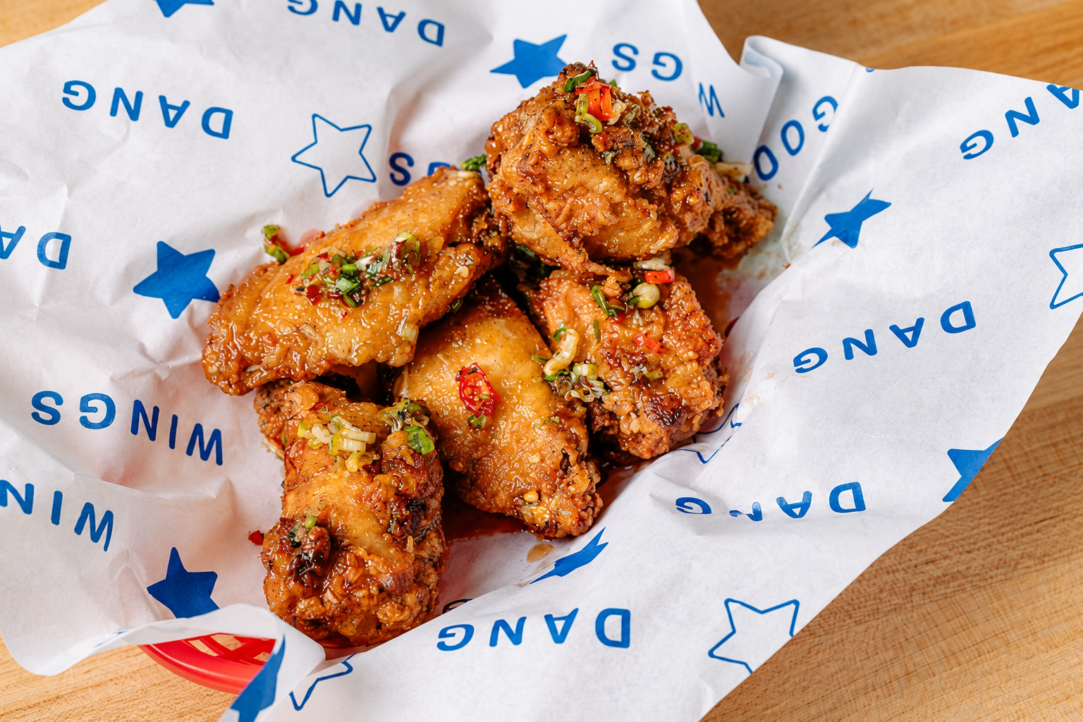 Glazed Dang Good Wings topped with scallions and sliced chilies on branded paper